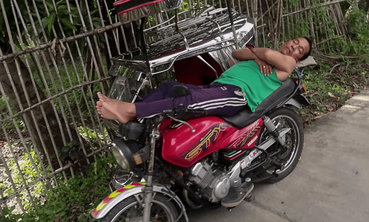 filipino man sleeping on top of his tricycle  in a typical barangay in the philippines